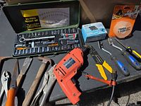 All items laid out: socket set open, drill, pliers, hammer, saw, stripper, chisels, tape, blade pack visible