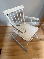 Front angled view of entire child rocking chair showing white distressed paint and rocker base