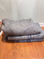 Three folded U-Haul recycled felt moving blankets stacked on floor