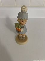 Front view of figurine showing girl, winter attire, carrots and base