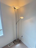 Full view of torchiere floor lamp standing in corner showing main shade, reading arm and base