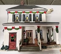 Front view of O’Well porcelain house showing porch, garland, wreaths and electrical cord
