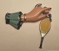 Brooch front showing hand, sleeve, bracelet, and dangling tennis racquet charm