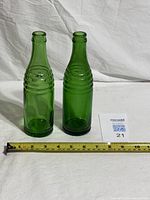 Pair of green glass bottles with tape measure for scale