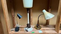 All three lamps on shelf: small black desk lamp, tall cream column lamp, brass and wood lamp with shade