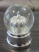Front view of snow globe showing silver crown inside glass dome on metal base