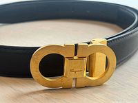 Full view of black leather belt coiled with gold-tone Gancini buckle facing forward