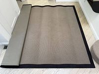 Area rug partially unrolled showing taupe field and black border