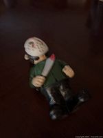 Front angled view of figurine lying face up showing white hockey mask, machete, green shirt, black pants