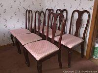 Six Queen Anne style mahogany dining chairs with coral pink satin upholstered seats arranged on carpeted floor near floral wallpapered wall.