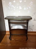Front view of wooden mid-century modern magazine rack with shelf showing overall structure and wear.