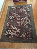 Area rug laid flat on wooden floor showing full leaf pattern and dark green border