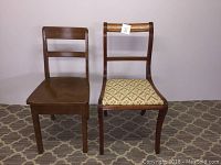 Two wooden chairs side by side against patterned carpet and plain background, one with fabric seat and curved backrest, the other with plain wooden seat and straight backrest.