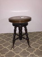 Front view of antique adjustable piano stool showing round wooden seat and dark polished turned wood legs with metal ball and claw feet with glass balls.