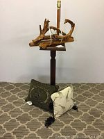 Photo of wood pedestal planter, craft driftwood lamp sitting on top, and two animal print cushions placed on the floor in front
