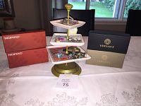 Photo showing jewelry tree with assorted bangles and bracelets along with Versace boxes and Nomad boxes on white tablecloth.
