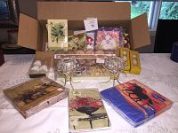 Showing the full lot contents including the two crystal candle holders, packs of designer napkins, votive candles box, and other small decorative items on table and inside open box.