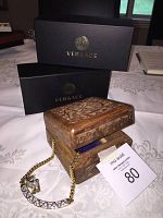 Opened carved wooden jewel box with FAC pave crystal necklace draped inside, Versace boxes in background