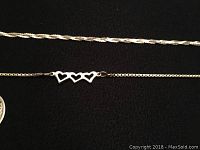 Close-up photo of the bracelet with three open hearts in silver and a fine linked chain on a black background.