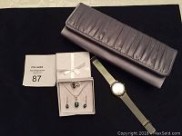 Photo showing overall lot contents including satin clutch, wristwatch, green stone jewelry set, and sale tag.