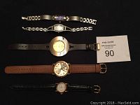 Lot of five ladies wristwatches arranged on black background, showing different faces and strap materials.