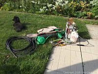Lot displayed outdoors on grass and patio, showing 50 ft black rubber hose coiled, green watering can, white and green handheld sprayers, various garden hand tools and a shovel.