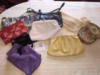 Full view of the collection of 9 ladies vintage purses, clutches and handbags including leather, macrame, fabric and bead detailed items arranged on a white surface.