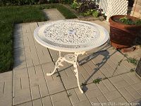 Overview of round cast metal patio table showing full table with three legs and central hole for umbrella.
