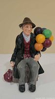Front view of The Balloon Man figurine showing seated man, balloons, bag