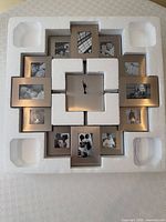 Clock in styrofoam packaging showing brushed silver frames, central dial, sample photos