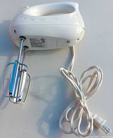 Side view of white hand mixer with cord and beaters attached