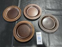 Four brown speckled stoneware dinner plates displayed on black surface