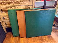 Three folded square tabletops leaning, two green, one brown
