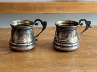Pair of tarnished silver cup holders with floral engraving and scroll handles