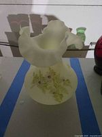 Front view of pale yellow-green Fenton vaseline glass vase showing floral painting and ruffled rim