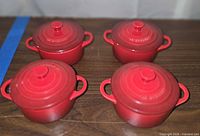 Four red Le Creuset mini cocottes with lids displayed