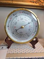 Front view of round brass aneroid barometer on wood stand showing dial details