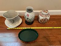 Group shot of planter with saucer, floral vase on wood stand, ginger jar, and green plate with tape for scale