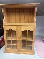 front view of solid wood display cabinet showing glass doors, open top shelf, wood knobs, natural finish
