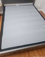 Box spring laid flat on bed frame, shows gray top and black edges