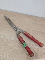 Full view of hedge shears with red wooden handles on wood surface
