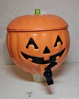 Front view of orange pumpkin drink dispenser showing face, lid, spigot and base