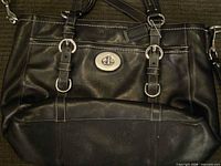 Front view of black Coach leather handbag with turn-lock clasp and buckle details