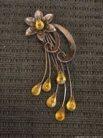 Front view of sterling silver brooch showing flower, scroll stem, five yellow teardrop dangles