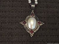 Close-up of sterling pendant showing white cabochon and red stones