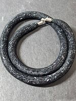 Coiled view showing entire black mesh glitter necklace and silver-tone end caps