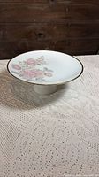 Angled side view showing pedestal base, floral pattern and gold rim