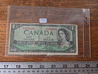 Full view of 1954 $1 banknote in sleeve with ruler for scale