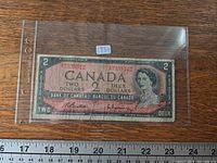 Full view of front of 1954 $2 note in sleeve next to ruler