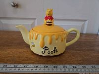 Left side view showing honey-drip design, text, spout and lid figurine
